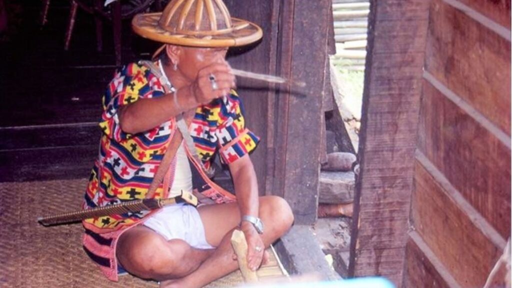 Idu Mishmi elder in traditional hat and attire performing a ritual indoors.