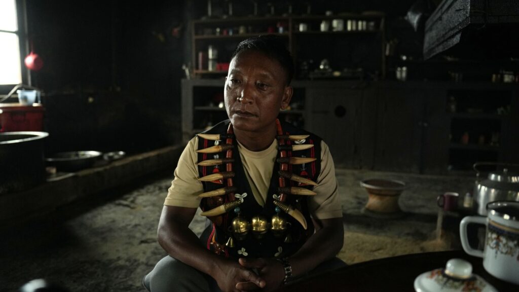Konyak man wearing traditional necklace sitting in dark kitchen.