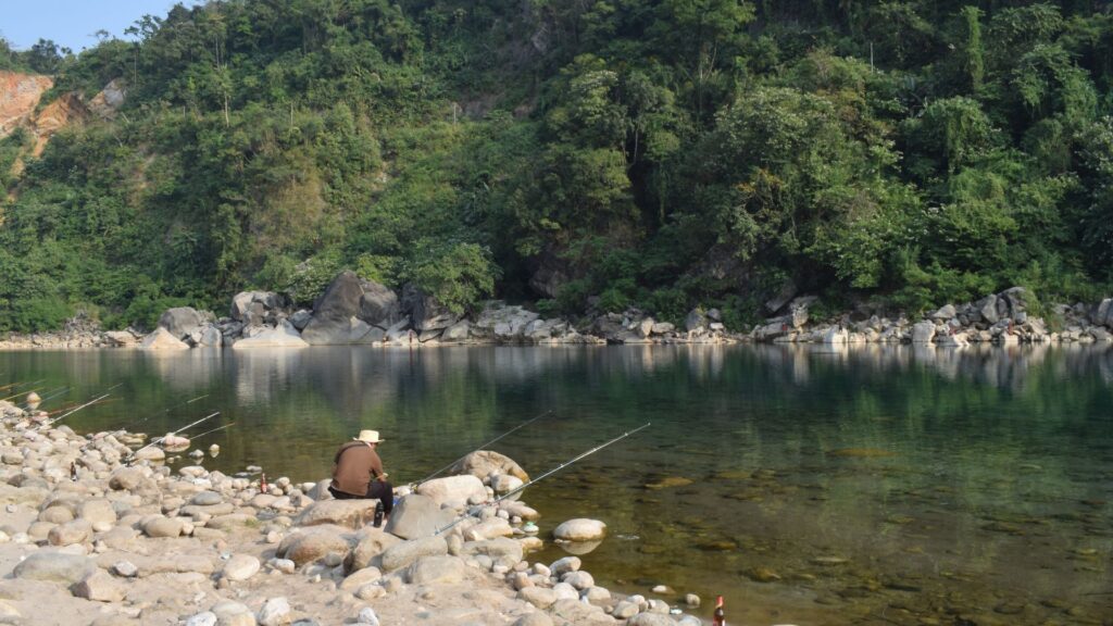 Man fishing from a rocky bank beside a clear green river