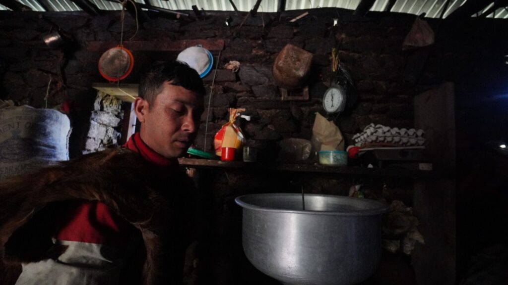 Brokpa man ladling food from a pot over a wood-fired stove