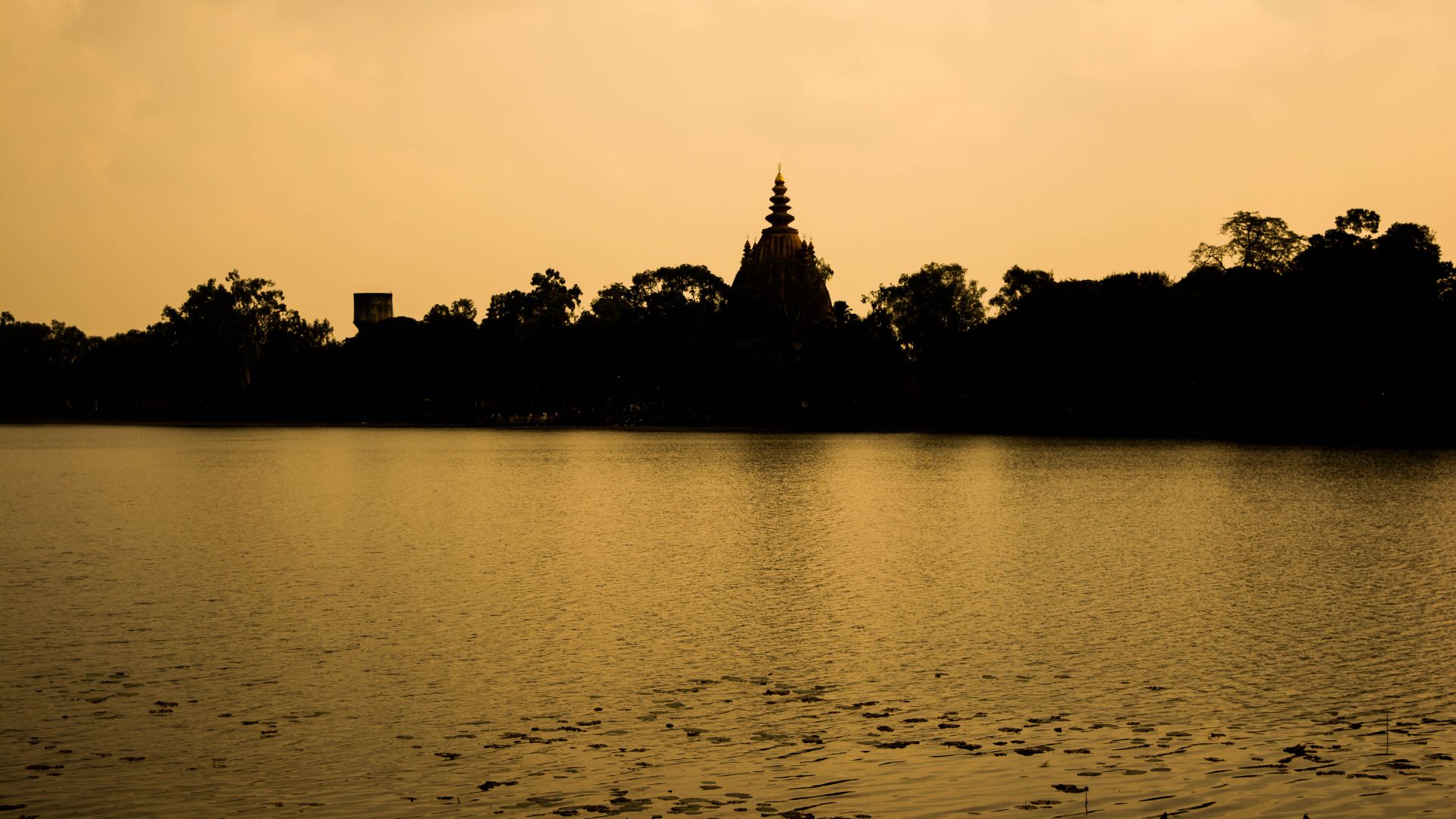 A temple and tree silhouettes across the water at sunset