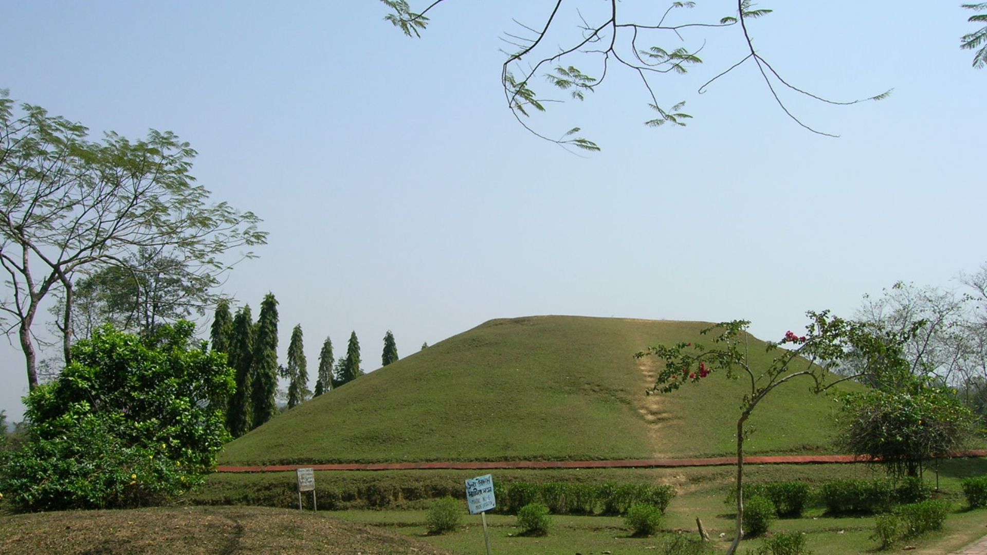 A grassy moidam rising gently above the surrounding landscape